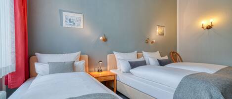 A hotel room with two beds, a nightstand with a lamp, and wall-mounted light fixtures.