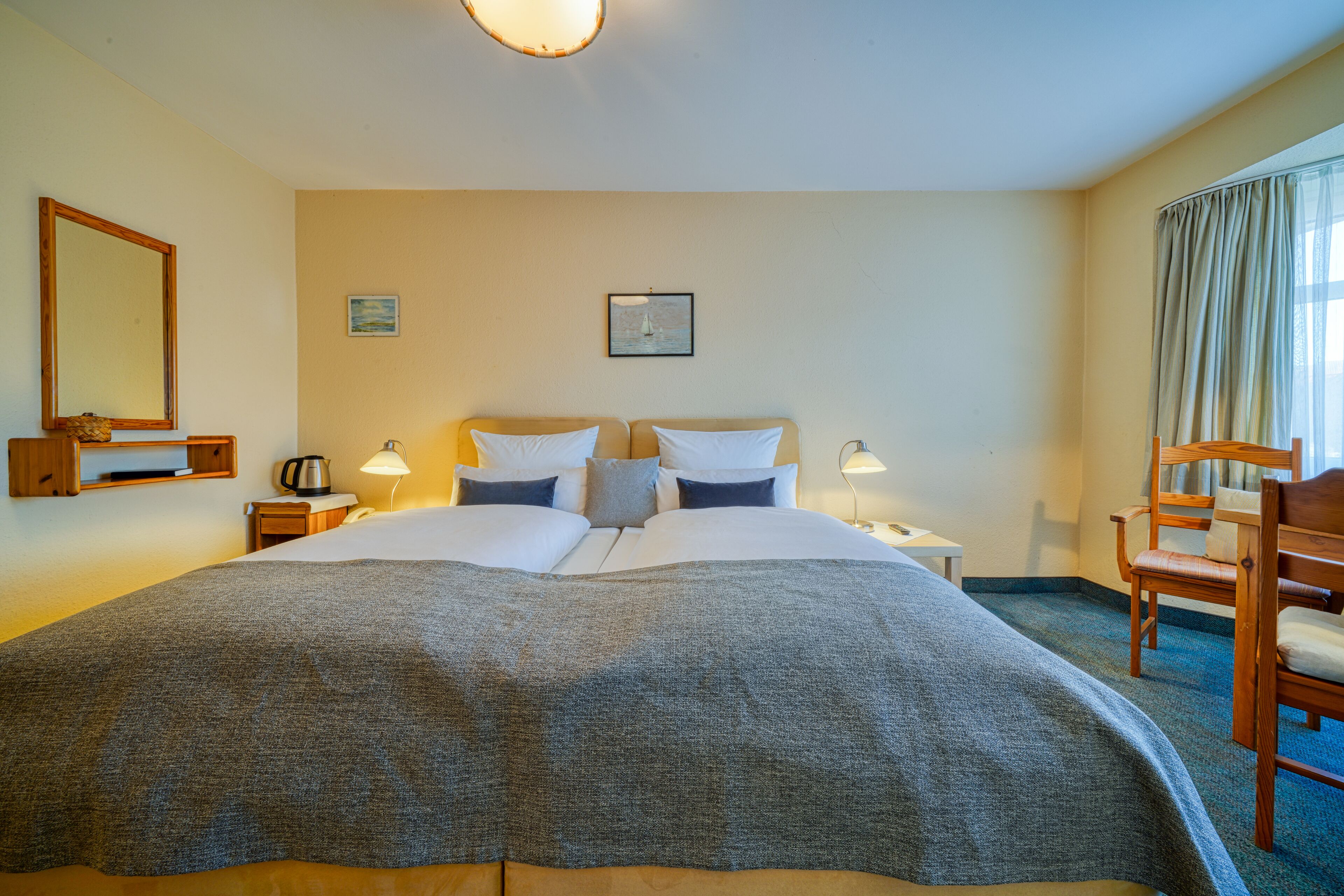A hotel room with a large bed, two bedside tables with lamps, a chair, and a window with curtains.