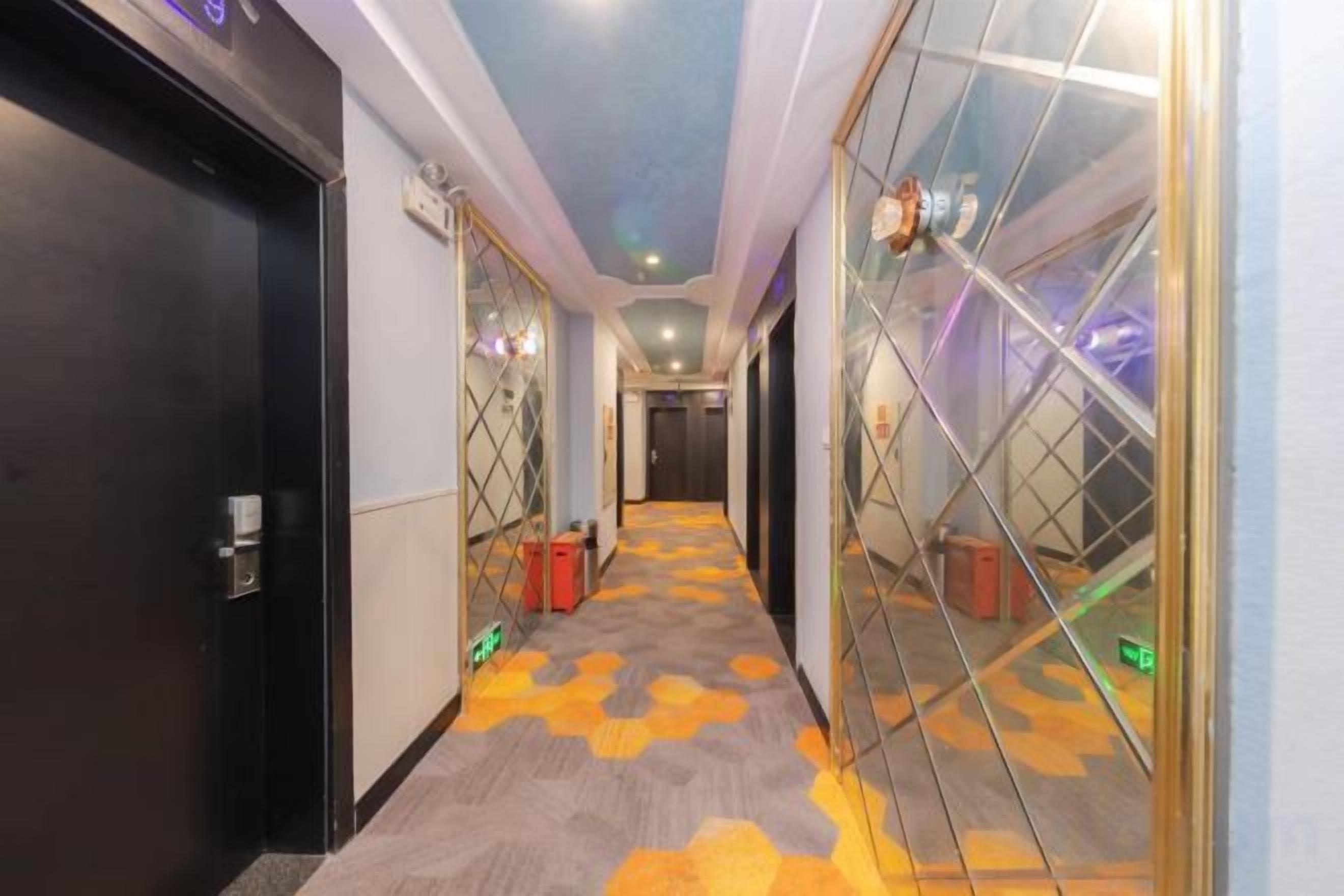 A hotel corridor with doors on both sides, a patterned carpet, and a ceiling with recessed lighting.