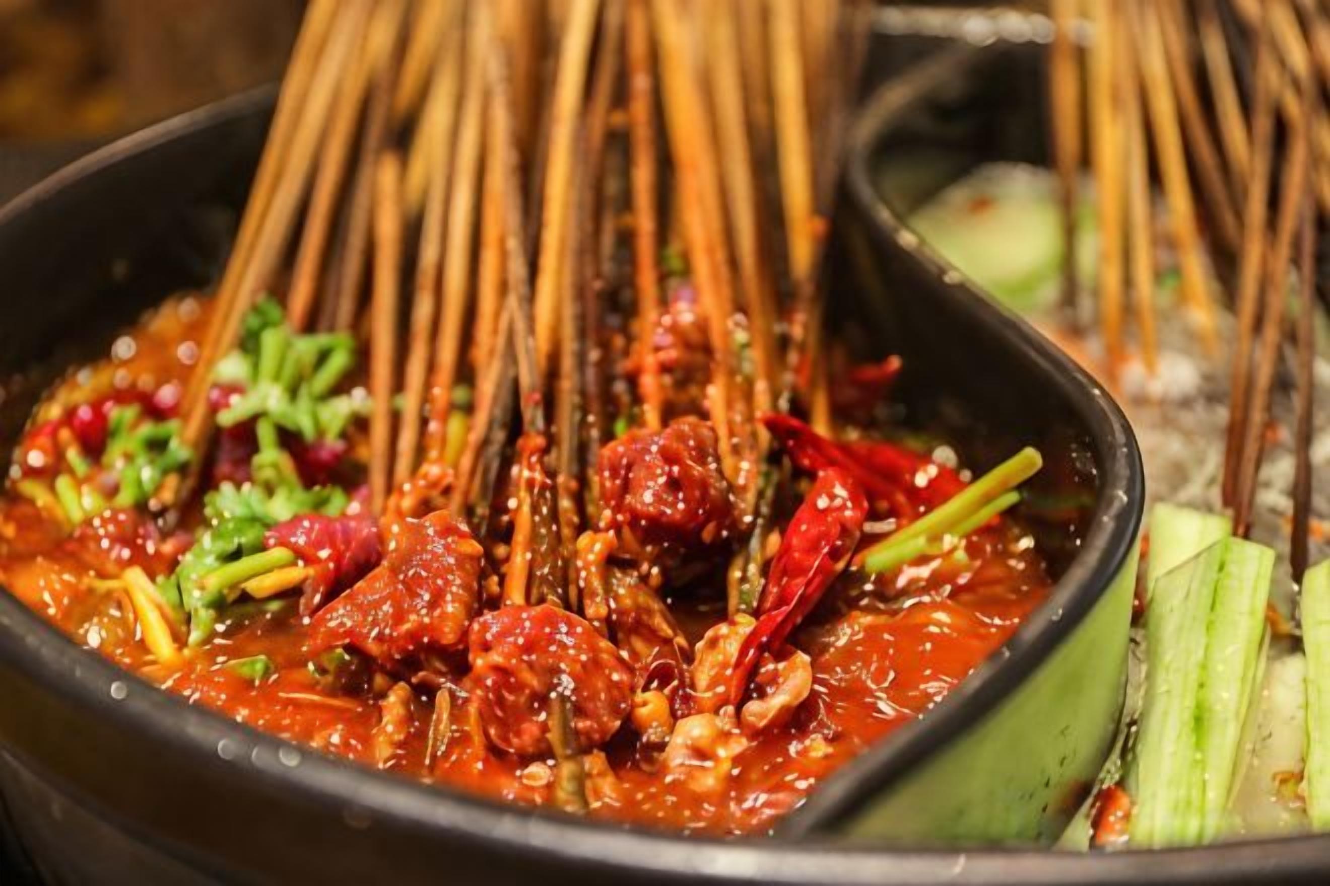 A hot pot with various ingredients and bamboo skewers.