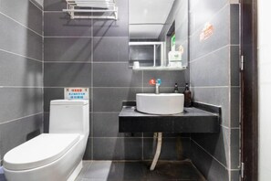 Et lille badeværelse med et hvidt toilet, en sort vask og et spejl over vasken.