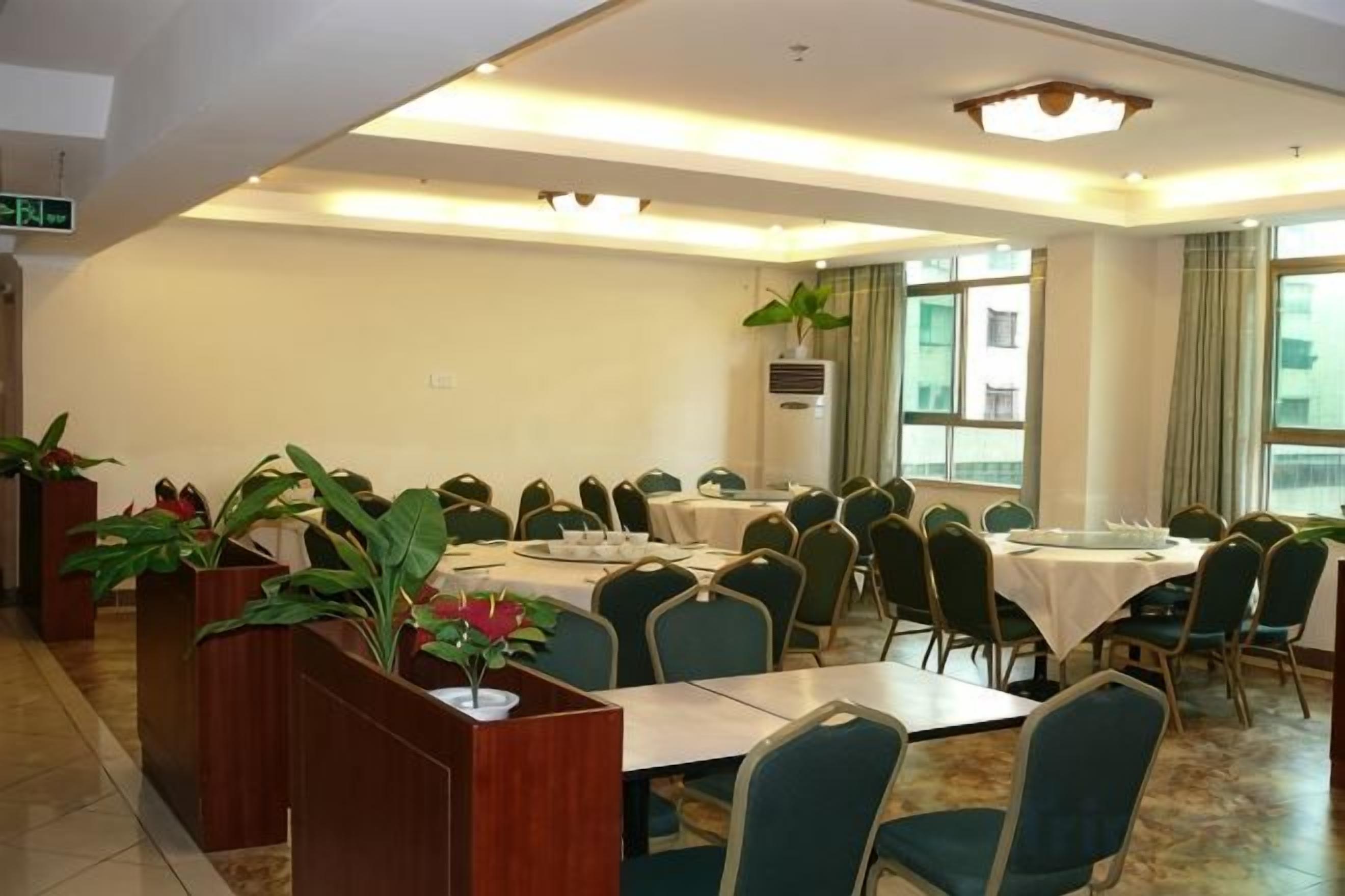 A conference room with multiple tables and chairs, large windows, and potted plants.