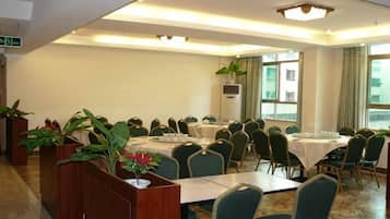 A conference room with multiple tables and chairs, large windows, and potted plants.
