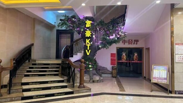 Vestíbulo de hotel con una escalera, un mostrador de recepción y un cartel que indica la zona de KTV.