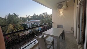 Ein Balkon mit Tisch und Stühlen, Geländer und Blick auf Palmen und Gebäude.