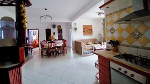 Una cocina amplia con estufa, un comedor con sillas y una mesa, y una sala de estar con sofá y televisor.