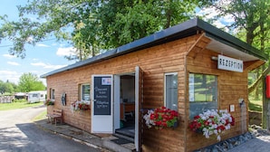 A wooden building with a reception sign, a bench outside, and flower boxes on the windows. - Vacation chalet on a campsite (Windeck)