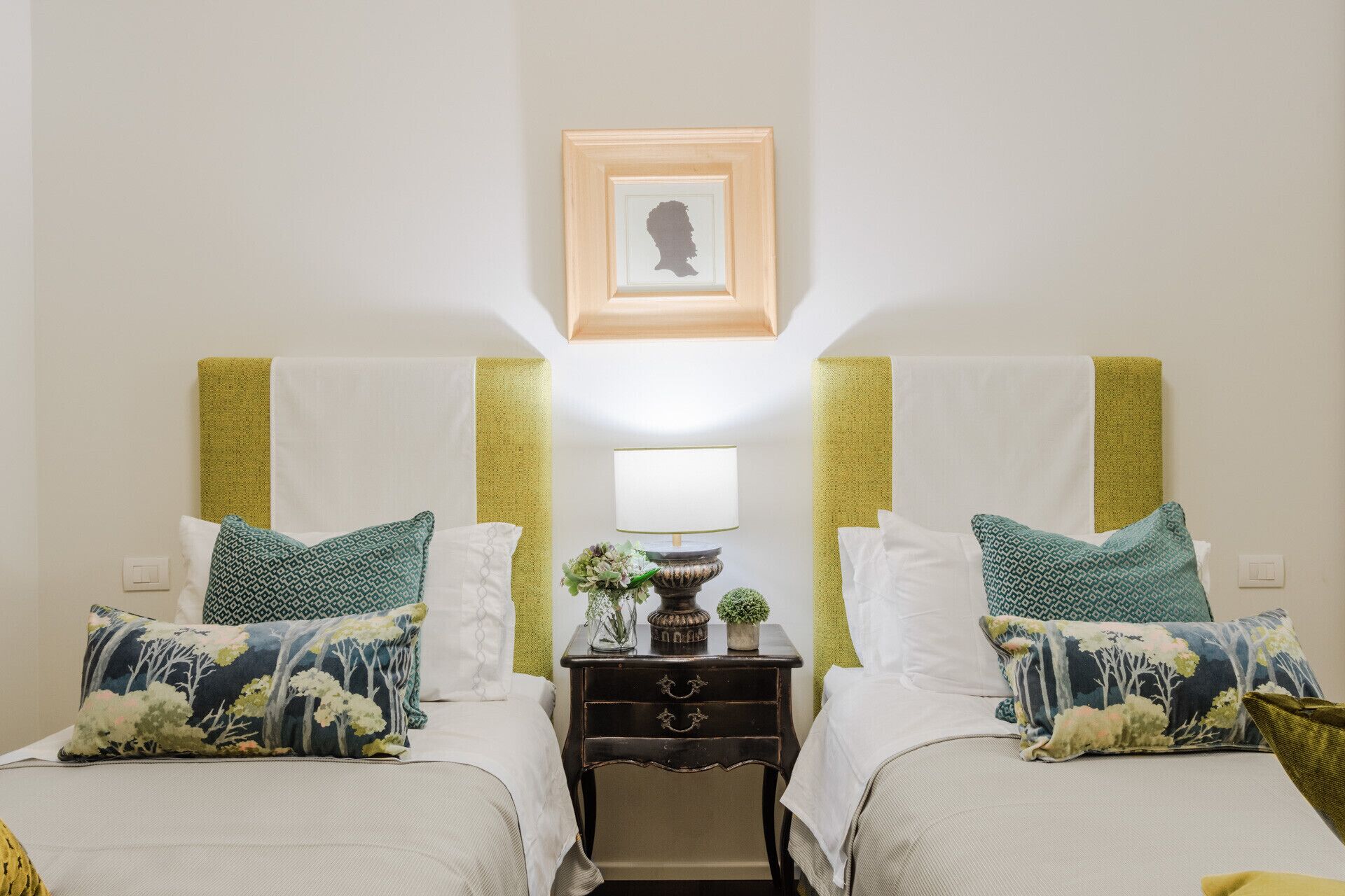 A hotel room with two beds, a nightstand with a lamp, and a framed picture on the wall.