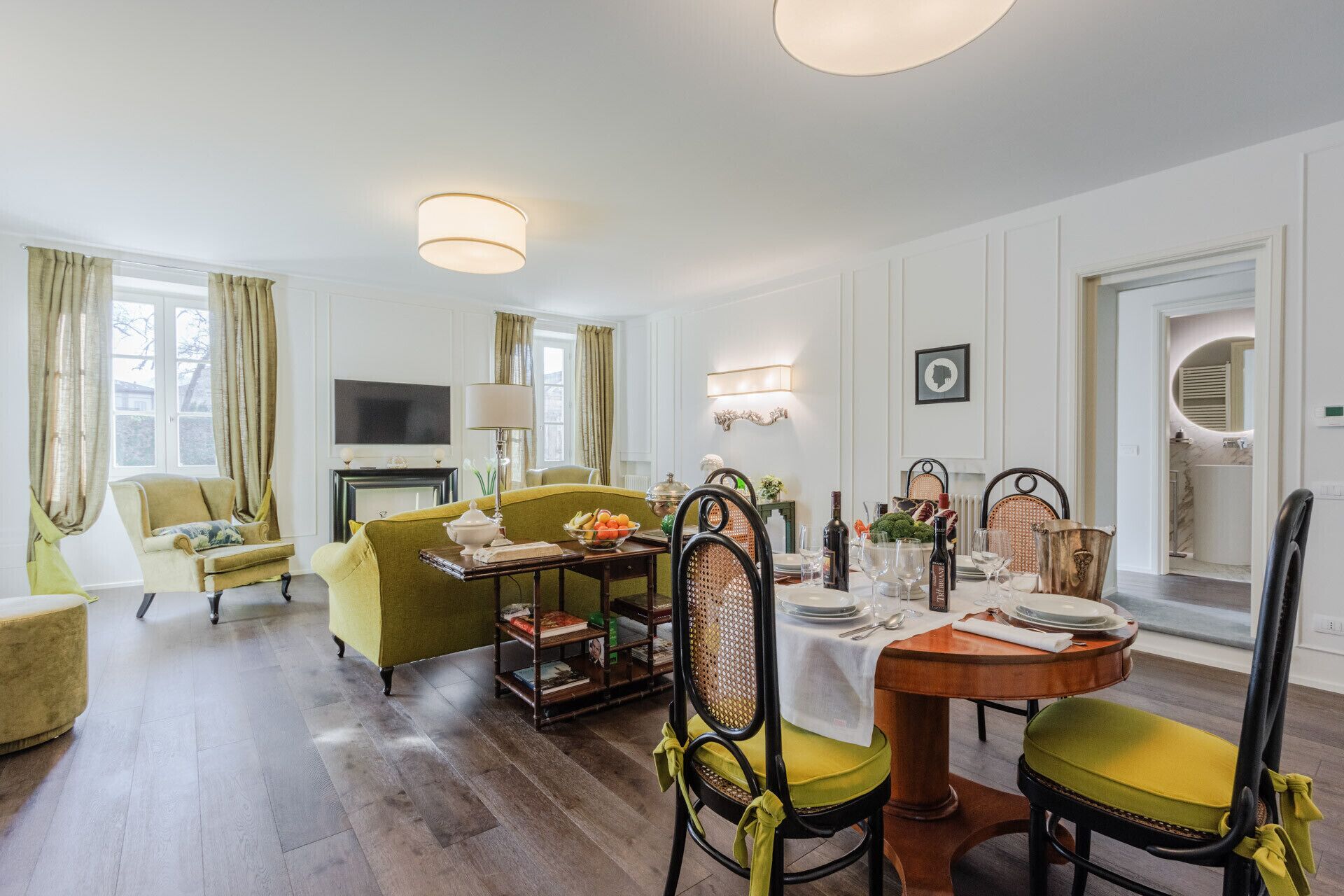 Een goed verlichte woonkamer met een groene bank, een eettafel voor vier personen en een televisie op de achtergrond.
