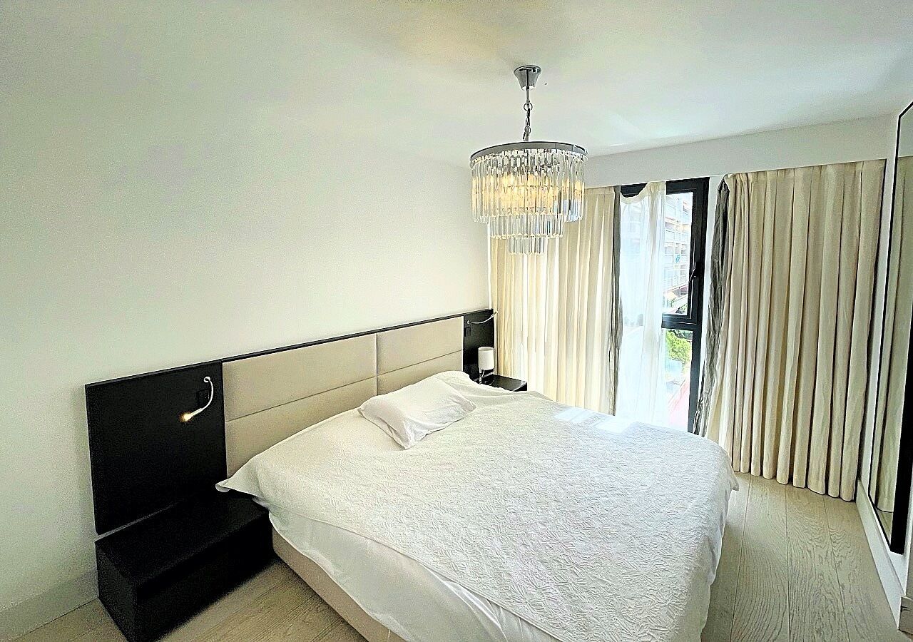 Ein Hotelzimmer mit einem großen Bett, einem Nachttisch, einer Stehlampe, einer Kronleuchter und einem Fenster mit Vorhängen.