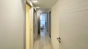 A narrow hallway with wooden flooring and white walls, leading to a room with a bed and a window with curtains. - Viva Riviera Carlton Riviera Luxury Collection (Cannes)