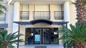 A building entrance with a glass door, palm trees, and a sign above the door. - Viva Riviera Carlton Riviera Luxury Collection (Cannes)