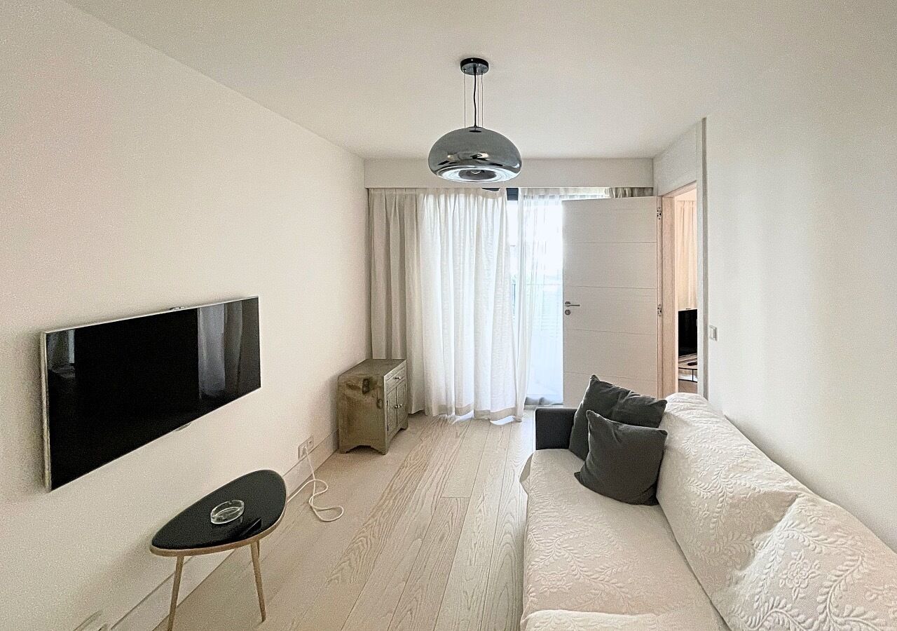 A modern living room with a flat-screen TV, a sofa, a small table, and a ceiling light.