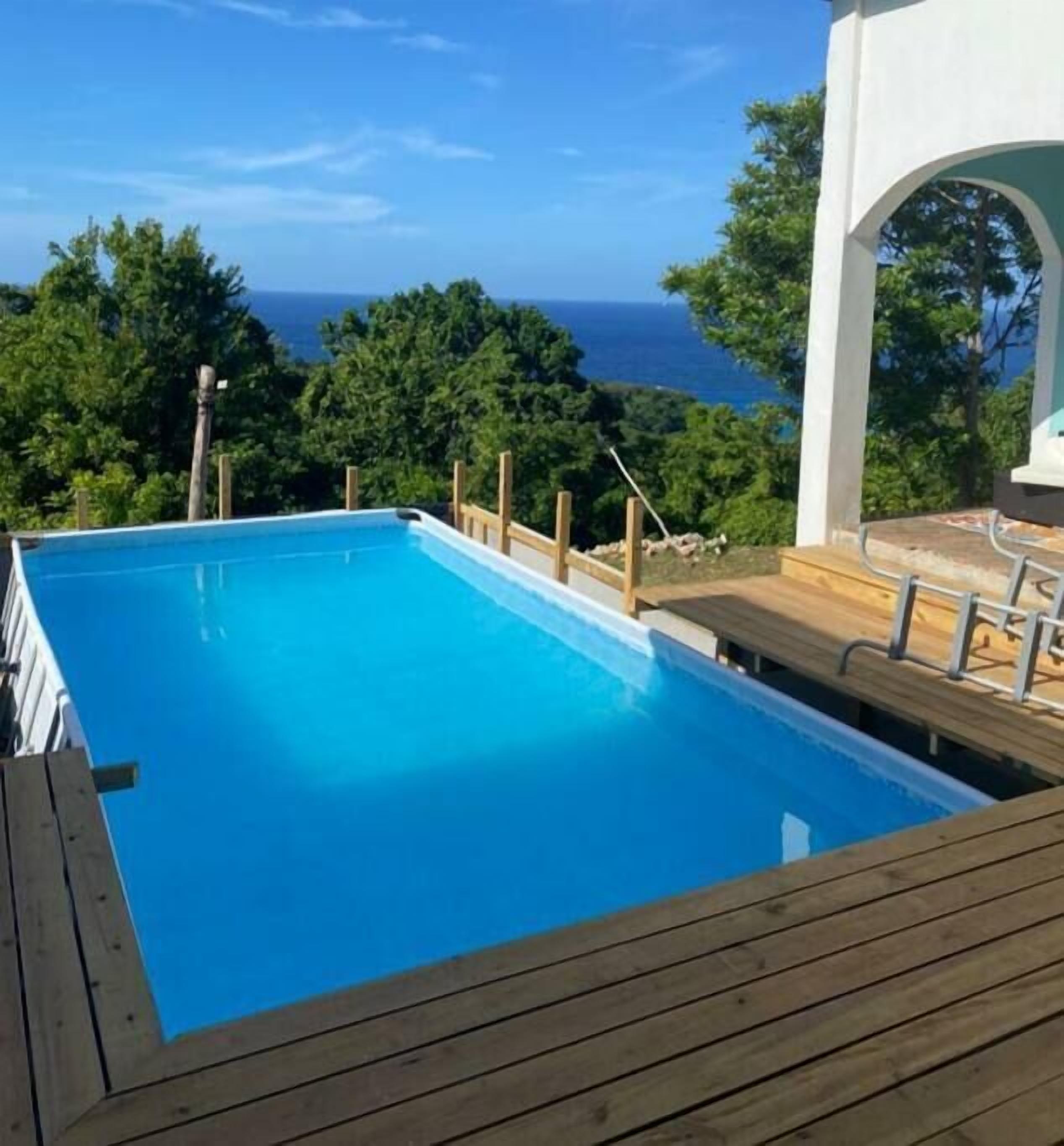 A clear blue swimming pool with wooden deck and a view of the ocean.