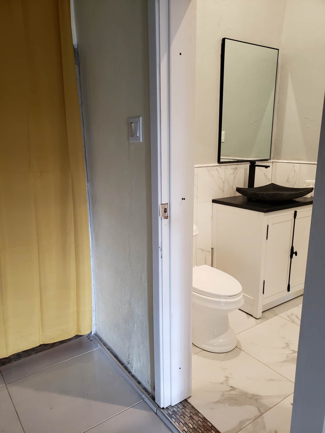 Ein Badezimmer mit einer weißen Toilette, einem schwarzen Waschbecken mit Marmorplatte und einem Spiegel darüber.