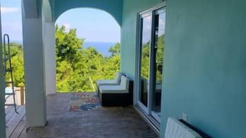 A balcony with a view of the ocean, a white cushioned bench, and a patterned rug.