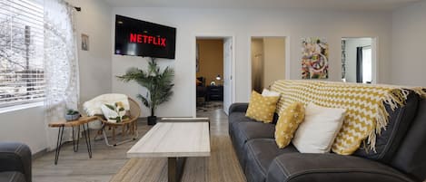 A living room with a black leather sofa, a coffee table, a TV mounted on the wall, and a potted plant.