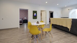 A modern living room with a dining area, featuring a round table and yellow chairs, a grey sofa, and a decorative wall hanging. - TWO Condos! Side by Side Curated Suites! Sleeps 18! Parking! (Nashville)