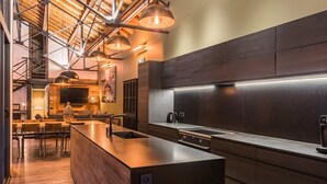 Une cuisine moderne dotée d’un îlot central, de meubles de rangement aux couleurs sombres et d’un éclairage suspendu.