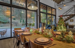 Un comedor con una mesa dispuesta para una comida, ventanas amplias y un árbol de Navidad decorado.