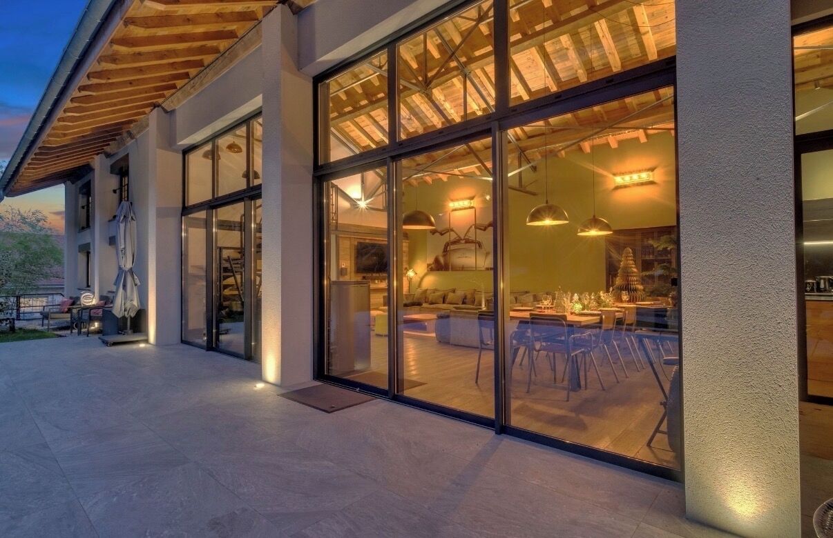 A modern building with large glass windows, a wooden ceiling, and an outdoor seating area.