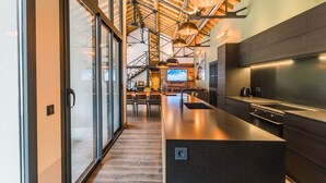 Une cuisine moderne dotée d’un grand îlot central, d’appareils électroménagers en acier inoxydable et d’un plafond haut avec des poutres apparentes.