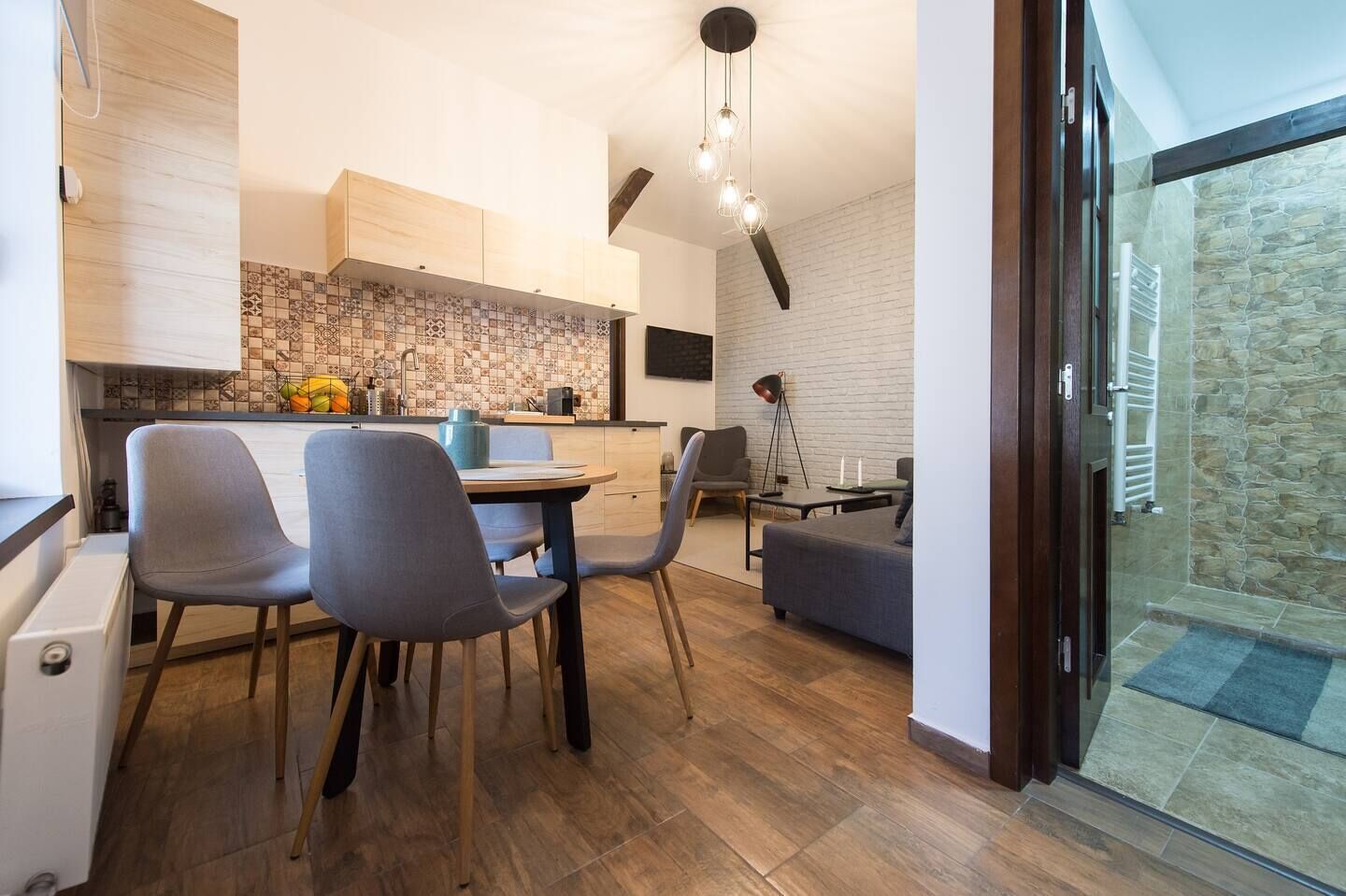 A modern kitchen with a dining area, wooden cabinets, and a stone wall.