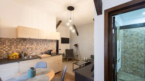 Eine kompakte Küche mit gefliestem Rücksprung, ein Essbereich mit Tisch und Stühlen, ein graues Sofa und eine Steinwand neben einer Glasschiebetür, die zu einer Steinterrasse führt.