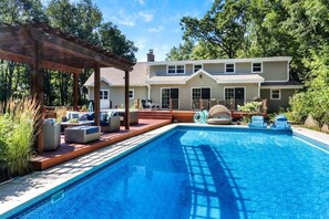Ein Garten mit Pool, Sitzgelegenheiten im Freien und einer Pergola.