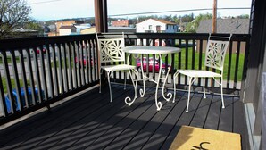 Una terraza de madera con dos sillas de metal blanco y una mesita redonda.
