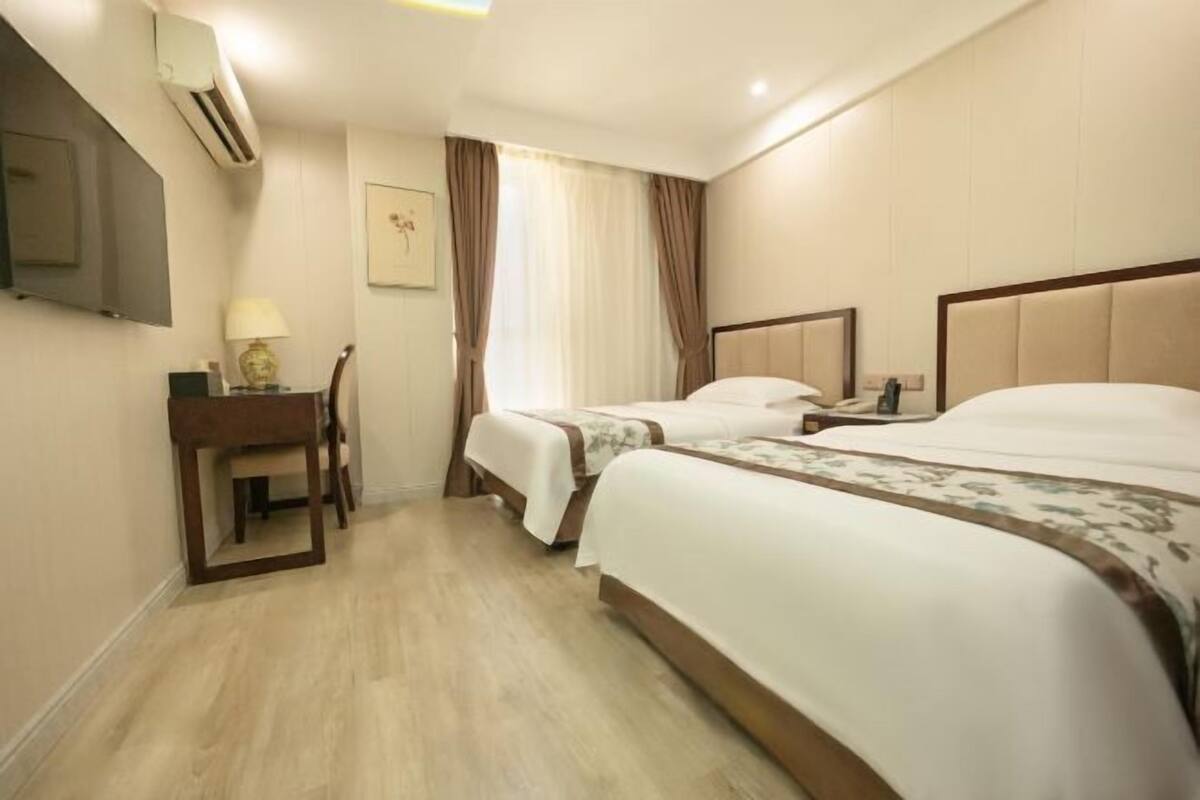 Une chambre d’hôtel avec deux lits, un bureau, une chaise, un téléviseur à écran plat et une fenêtre avec des rideaux.