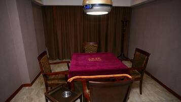 A hotel room with a dining table, four chairs, a small side table, a floor lamp, and a curtain backdrop.