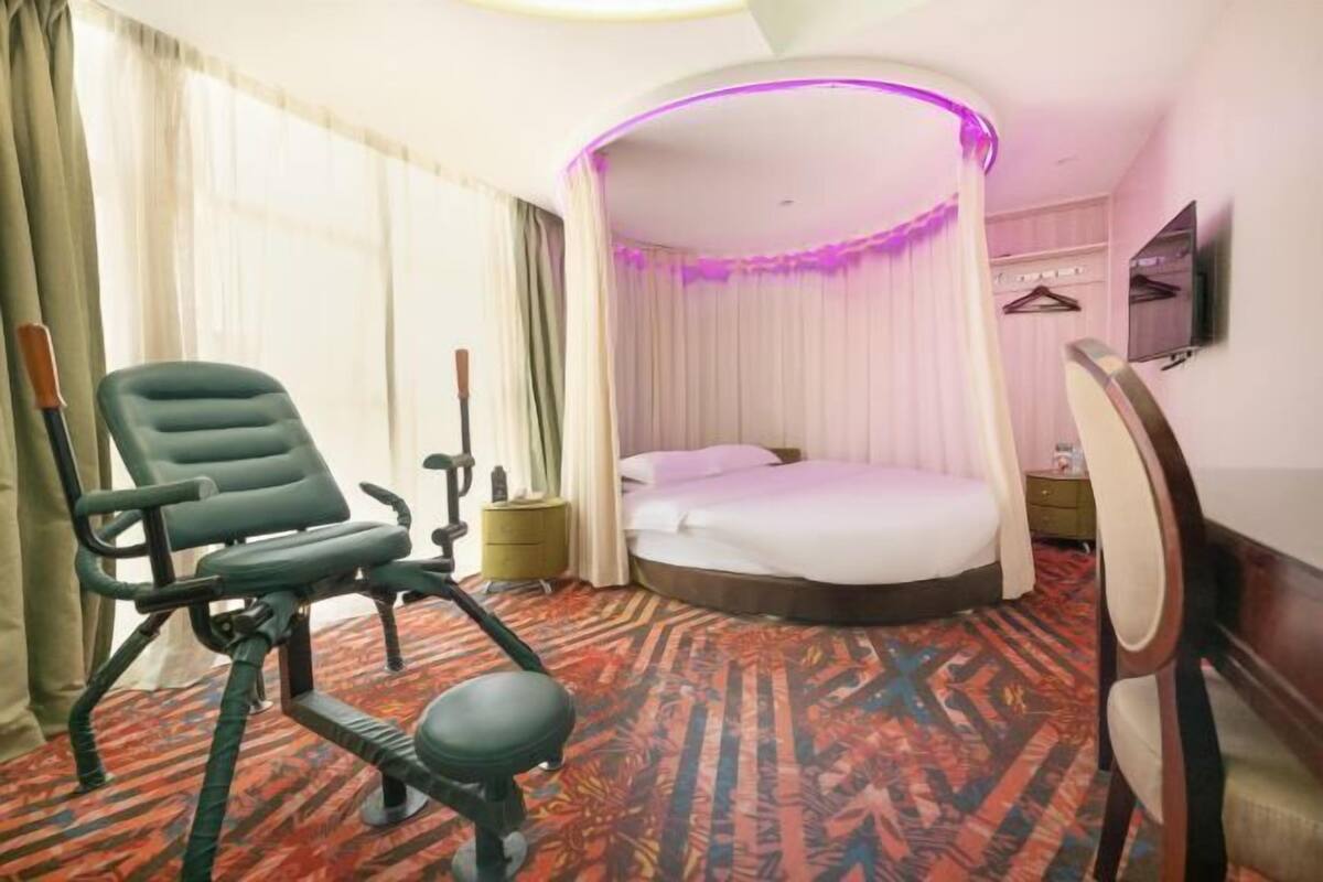 Une chambre d’hôtel avec un lit, une chaise, une petite table, un téléviseur et un rideau.