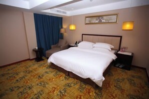 Ein Hotelzimmer mit einem großen Bett, einem Sessel, einem Schreibtisch und einer Lampe.