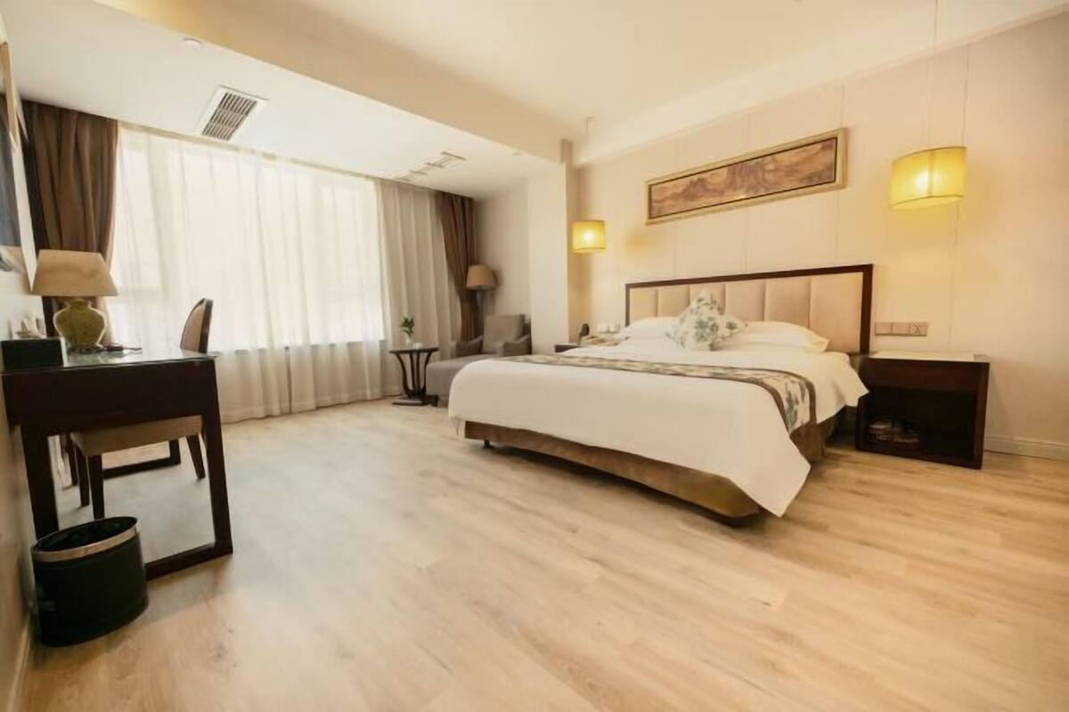 Une chambre d’hôtel avec un lit, des tables de chevet, un bureau, une chaise, une lampe et un tableau au mur.