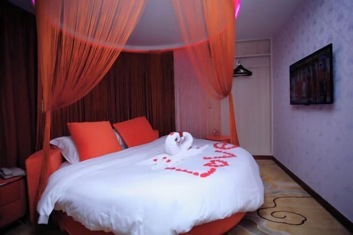 Ein Hotelzimmer mit Bett, roten Vorhängen, einem Bild an der Wand und einem gemusterten Boden.