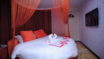 A hotel room with a bed, red curtains, a painting on the wall, and a patterned floor.