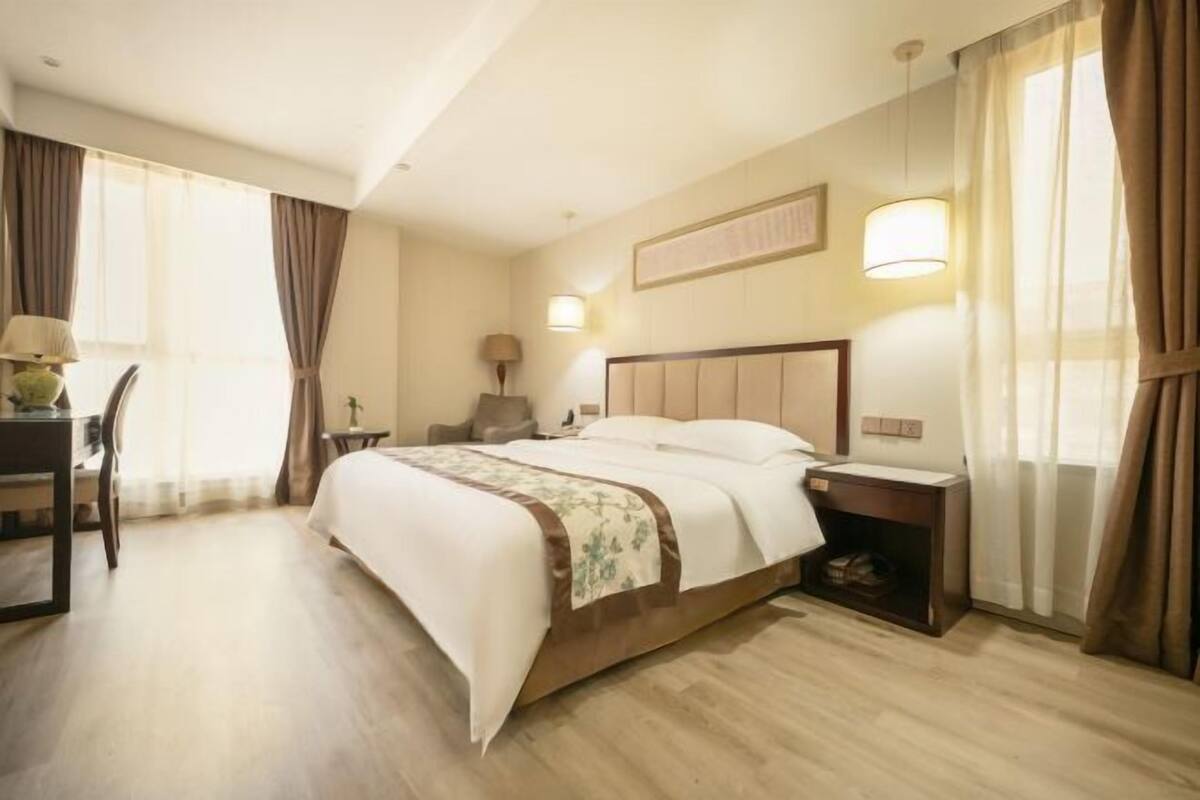 Une chambre d’hôtel avec un lit, une table de chevet, une lampe, une chaise et des rideaux.
