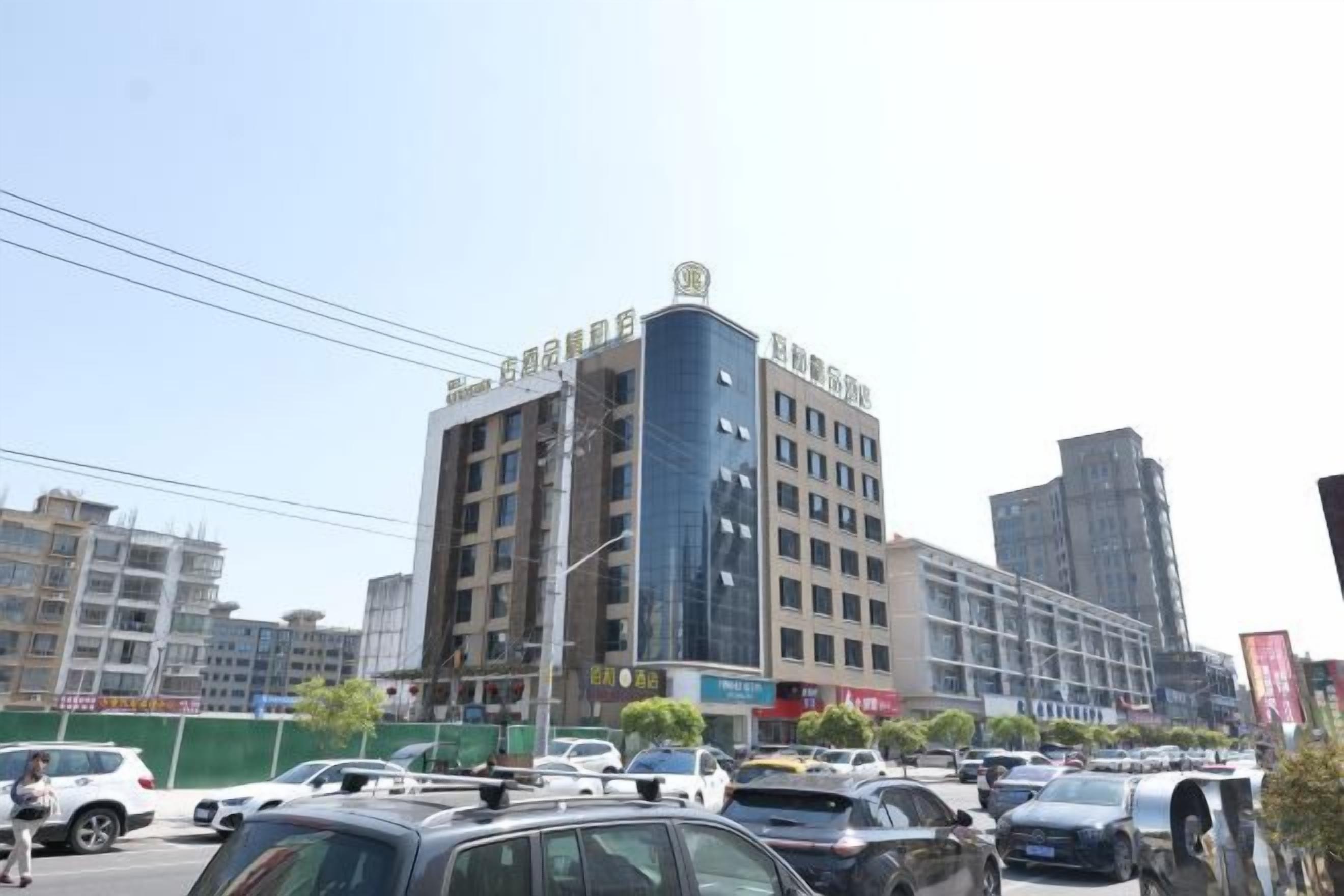 A multi-story building with commercial signage on the ground floor, surrounded by parked cars and other buildings.