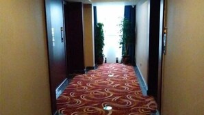 A hotel hallway with a patterned carpet, potted plants, and doors on either side. - Baihe Boutique Hotel (Yueqing Beibaixiang Store) (Yueqing)