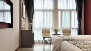 A hotel room with a bed, two chairs, a small table with a plant, and a TV on the wall.