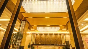 A hotel lobby with a wooden reception desk, a large chandelier, and a decorative wall panel.