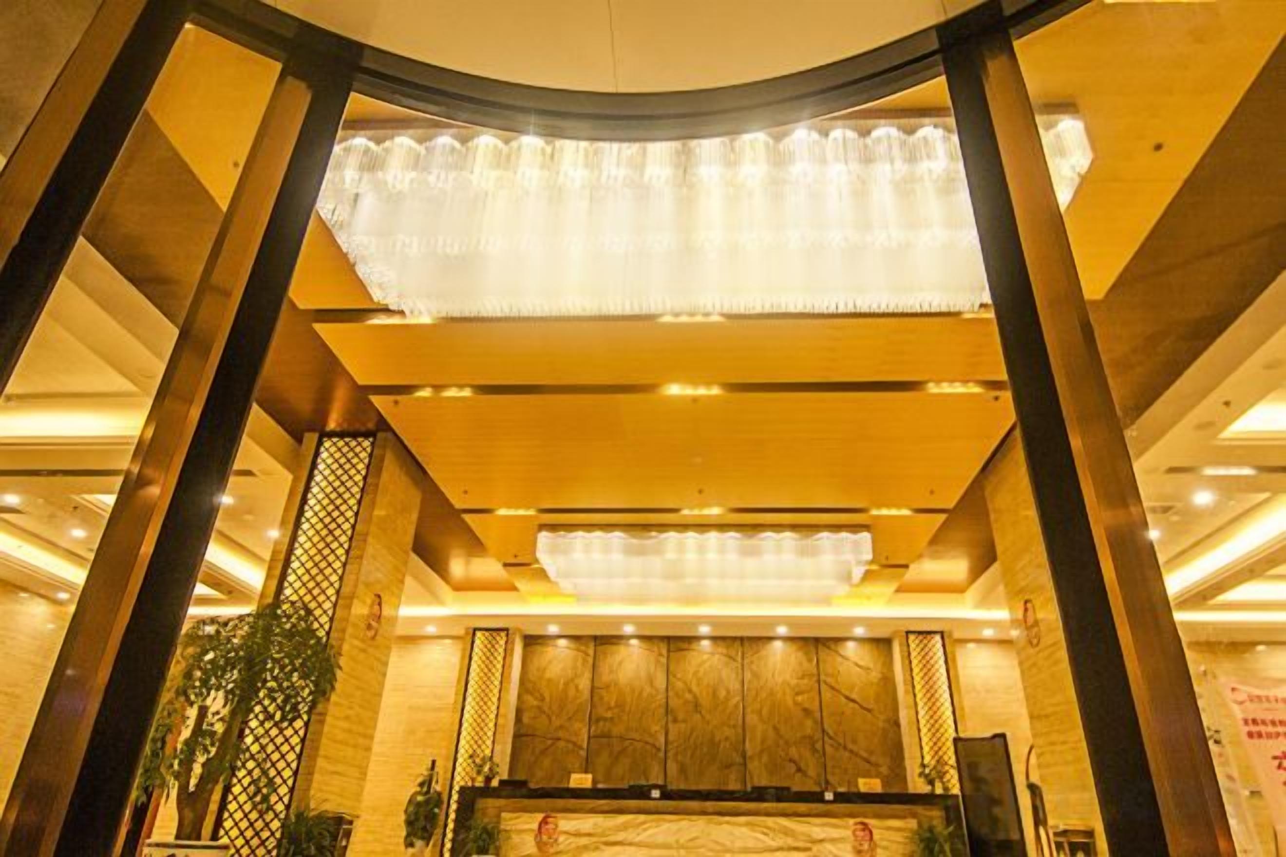 A hotel lobby with a reception desk, a chandelier, and a plant.