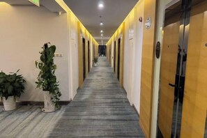 Un pasillo de hotel con puertas a ambos lados, plantas en macetas y suelo alfombrado.