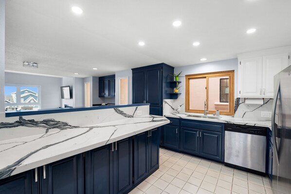 A modern kitchen with dark blue cabinets, a white marble countertop, and stainless steel appliances. - 3446 O - Blue Haven Beach House (Oxnard)