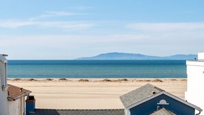 A coastal view with a sandy beach, a clear blue sea, and distant mountains.