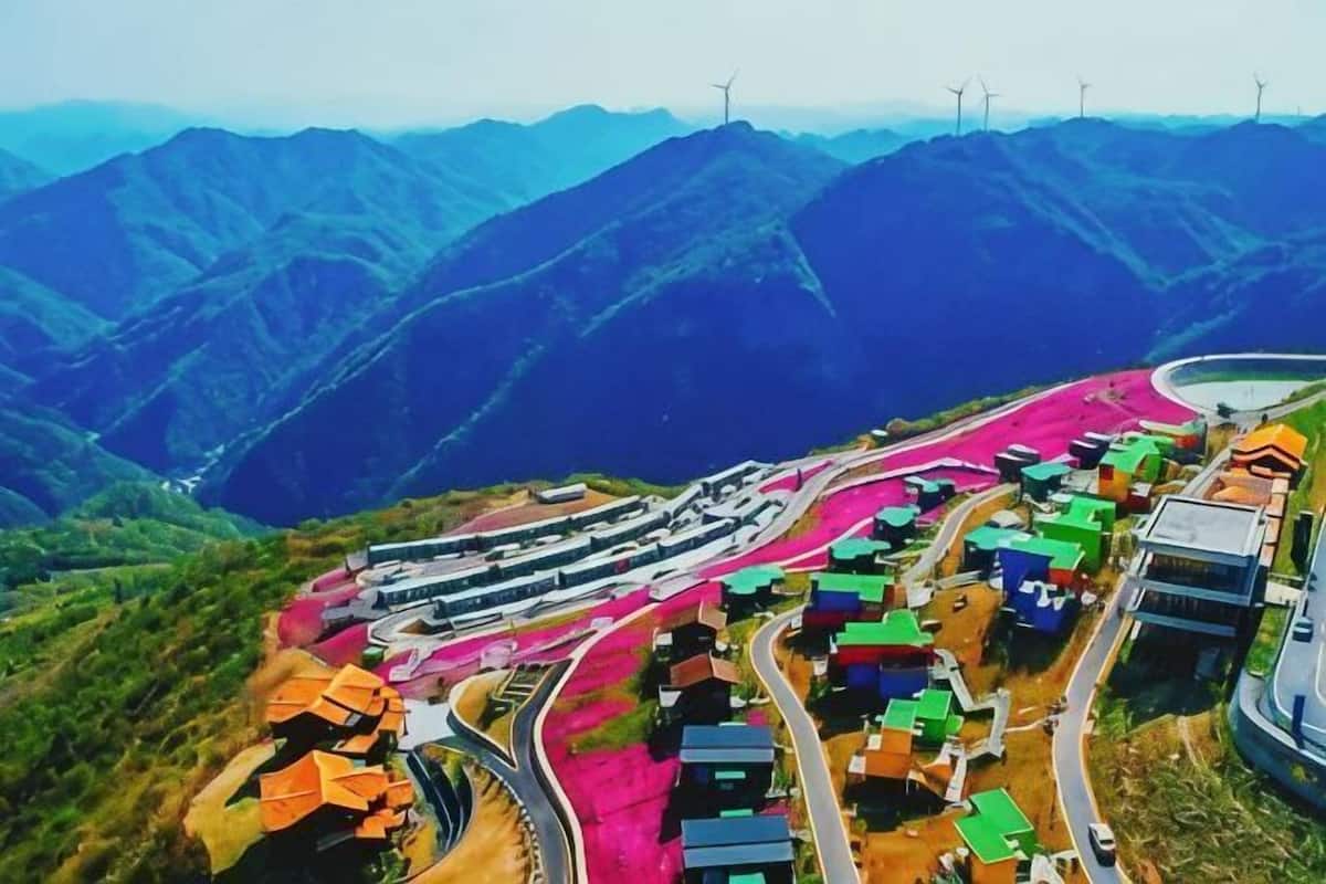 A winding road through a mountainous area with colorful buildings and wind turbines in the background.