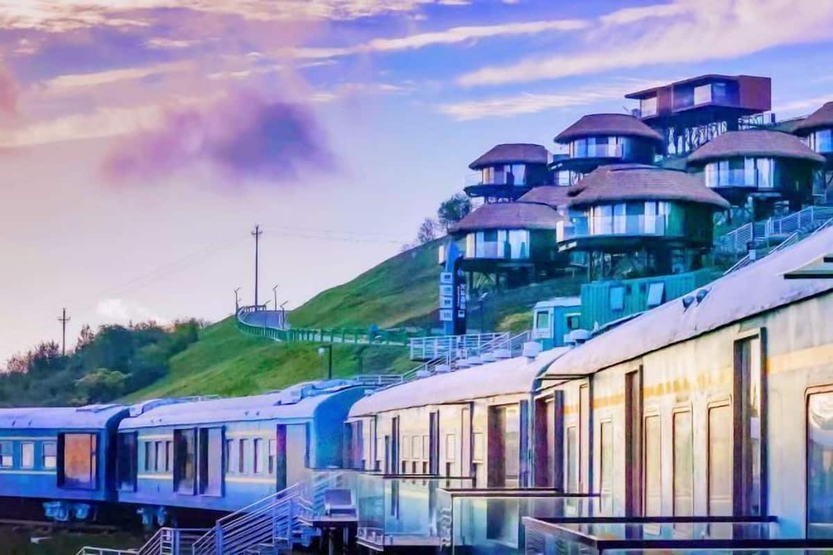 A train station with multiple train cars and a hillside with buildings.