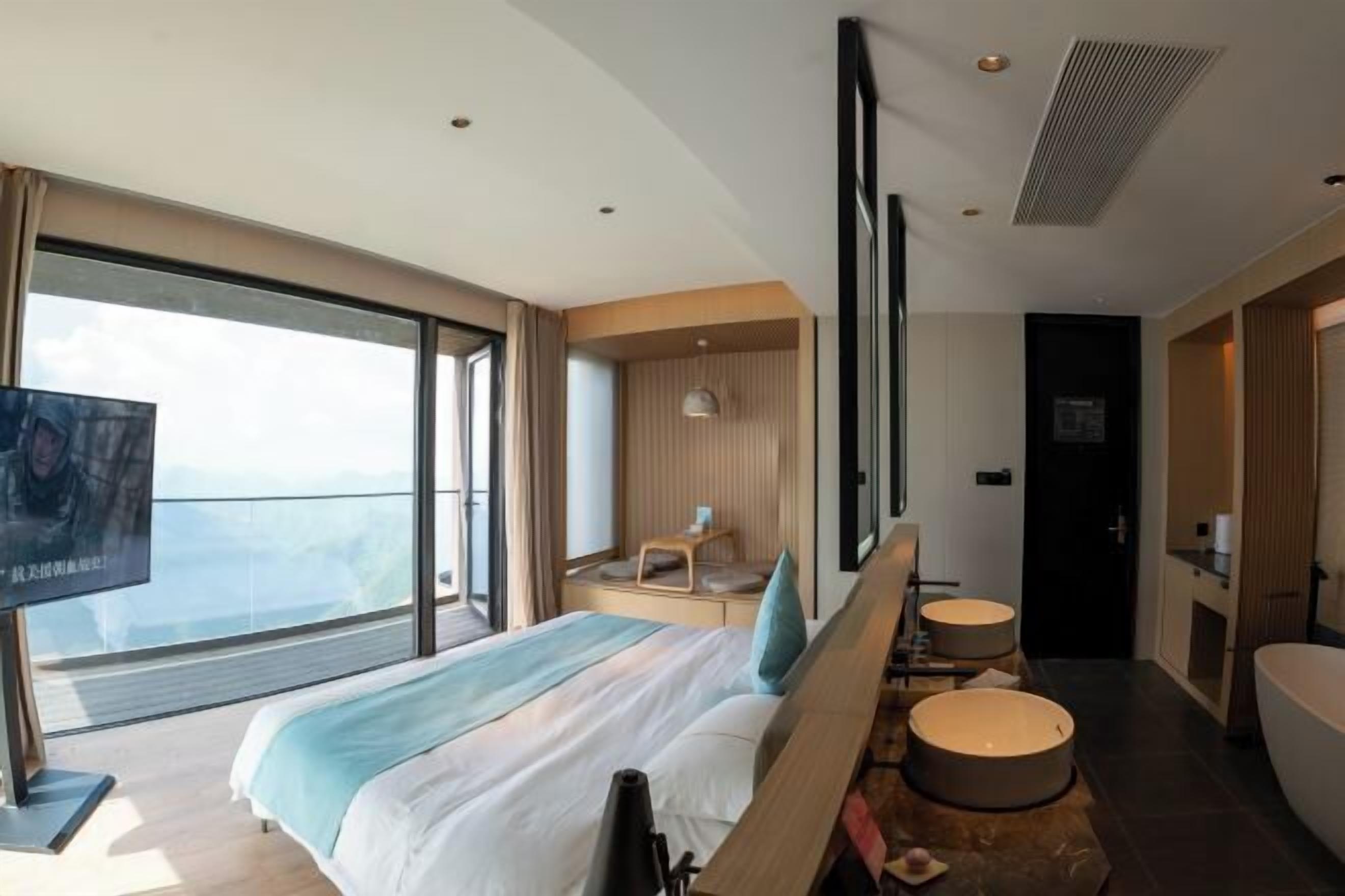 Quarto de hotel moderno com cama grande, televisão, área de estar e banheiro.