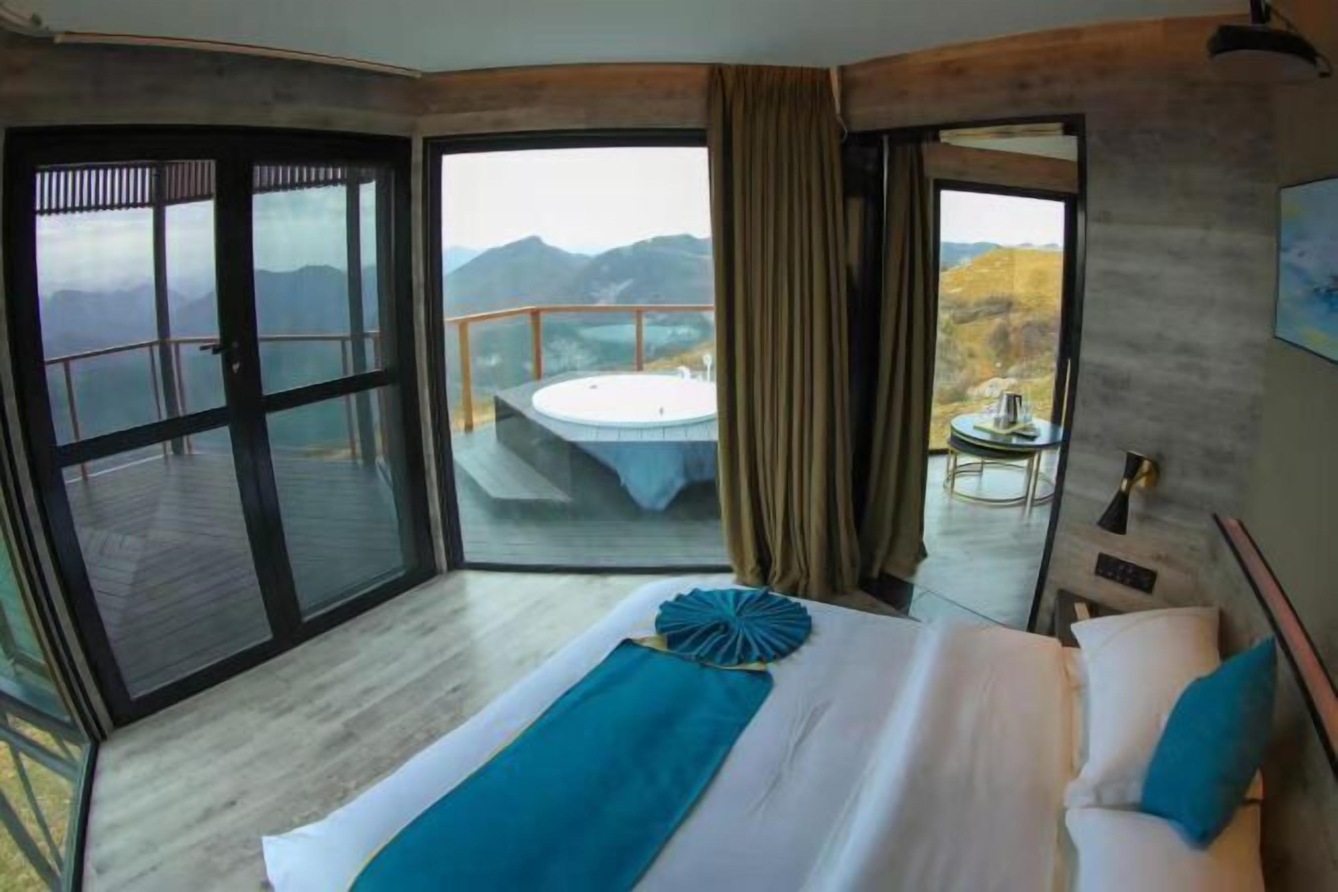 A bedroom with a large bed, a view of mountains, and a hot tub outside.